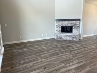Model Home A modern living area with gray wood flooring, a white brick fireplace, and soft neutral walls.