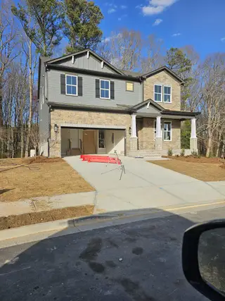 Street view An elegant craftsman-style home with brick and gray siding in The Paddocks at Doc Hughes by Beazer Homes (Buford, GA).