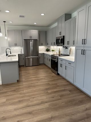 A modern kitchen featuring sleek gray cabinets, stainless steel appliances, and warm wood flooring.