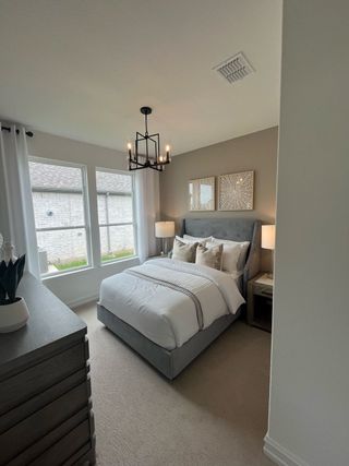 A cozy bedroom featuring a plush bed, modern chandelier, and soft lighting. Neutral tones create a relaxing atmosphere.