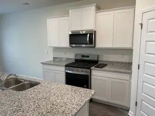 A modern kitchen featuring granite countertops, sleek white cabinets, and stainless steel appliances.