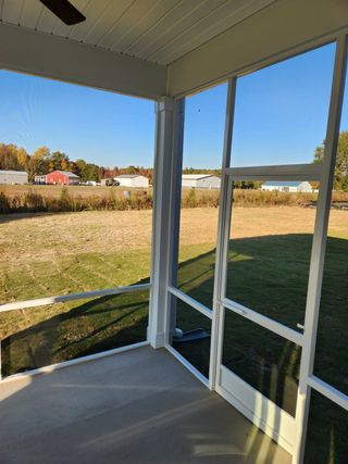A cozy screened-in porch with a serene view of fields and distant homes, offering a peaceful outdoor retreat.
