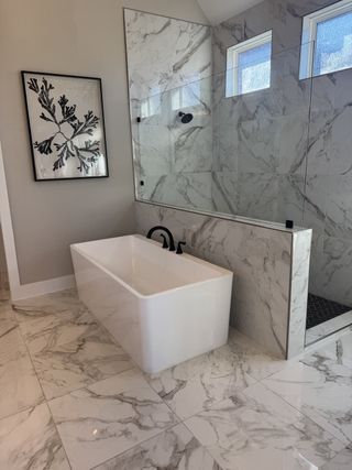 A luxurious bathroom featuring marble tiles, a sleek bathtub, elegant glass shower, and modern artwork.