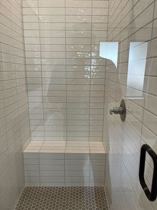 A sleek shower with white subway tiles, a convenient bench, and modern fixtures for a stylish bath experience.
