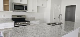 A modern kitchen with sleek granite countertops, stainless steel appliances, and elegant white cabinetry.