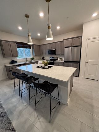A modern kitchen with sleek pendant lighting, gray cabinetry, and an island with black stools and stainless appliances.