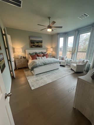 Model Home A serene bedroom with soft blue walls, a plush white bed, and a cozy sitting area by large windows, offering a tranquil retreat.