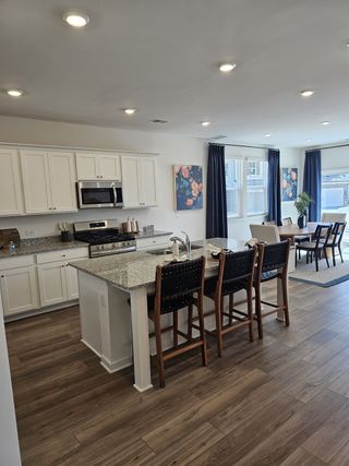 Modern kitchen with granite island, stylish bar seating, and wood flooring. Open living area with large windows and elegant decor.