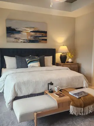 A cozy bedroom featuring a plush bed, elegant artwork, and warm lighting, creating a serene ambiance.