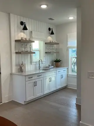 A chic kitchenette with white cabinetry, floating shelves, and ambient lighting, perfect for modern living.