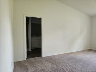 Model Home A spacious bedroom with plush carpeting and a doorway leading to an adjacent bathroom space, featuring clean white walls.