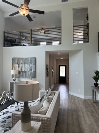 A modern living room with high ceilings, wood flooring, and stylish decor, featuring an open loft space above.