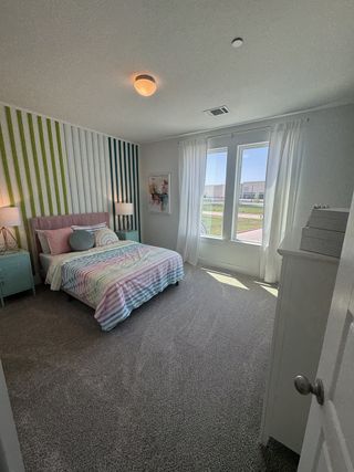 A cozy bedroom featuring a pastel-striped bedspread, accent wall, and large window with sheer curtains for natural light.