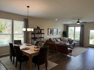 Model Home A bright living and dining area with dark hardwood floors, featuring a wooden dining table with place settings, a gray sectional sofa, leather armchairs, and framed artwork.
