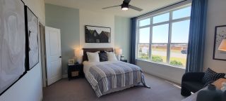 A cozy bedroom featuring a large window, modern art, and elegant furnishings with a neutral color palette.