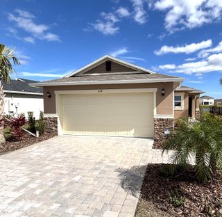 Street view A charming tan home with stone accents and a landscaped yard at Gardens at Waterstone II by KB Home (Palm Bay, FL).