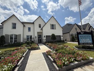 Street view Charming white brick home with manicured flower beds in Sienna - 60' by Westin Homes, Missouri City, TX.