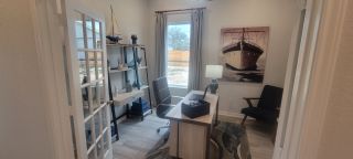 A cozy home office with nautical decor, featuring a desk, chair, and ample natural light through a large window.