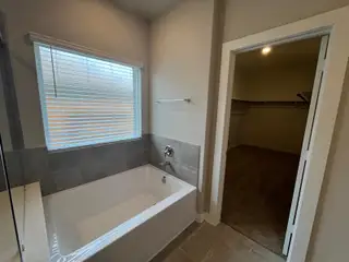 A modern bathroom featuring a sleek bathtub, tiled walls, and an adjoining walk-in closet for ample storage.