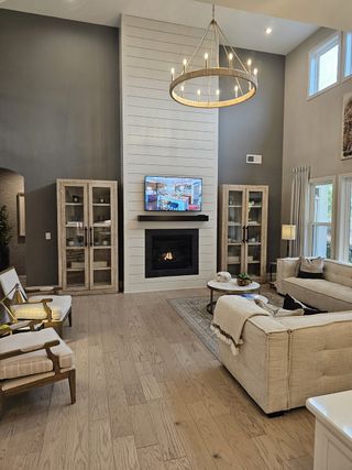 A bright and airy open-concept living space with soaring windows, contemporary chandeliers, and warm wood floors.