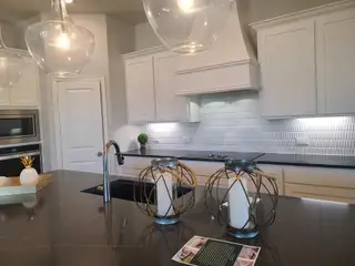 A modern kitchen featuring sleek cabinetry, textured backsplash, elegant pendant lighting, and a dark marble countertop.