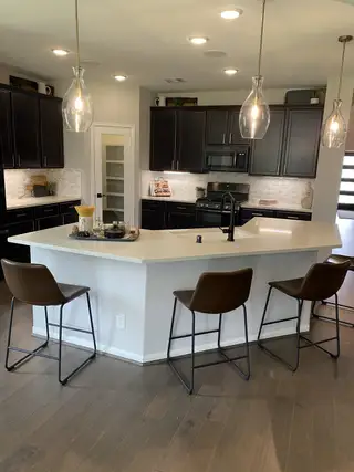 A modern kitchen with dark cabinets, a white countertop island, and stylish pendant lights.