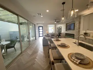 Model Home A modern open-concept living area with sliding glass doors, herringbone floors, and elegant pendant lighting.