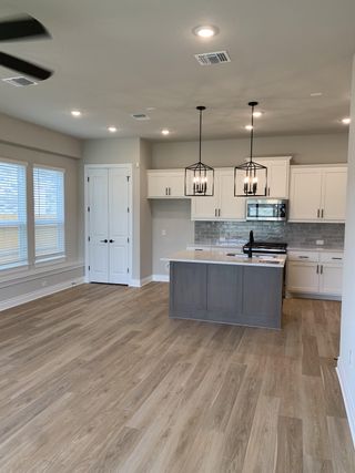 An open kitchen with sleek pendant lighting, white cabinetry, and light wood floors.