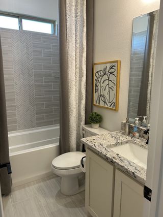 A cozy bathroom with a granite countertop, elegant tiling, and modern decor accentuated by a stylish plant and artwork.