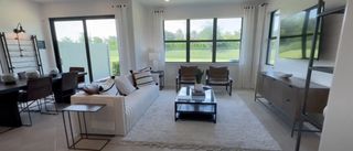 A bright living room with a white sofa, stylish chairs, and large windows overlooking a green landscape.