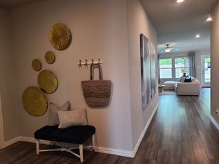 Model Home A modern hallway with decorative wall art, cozy bench, and an inviting living area featuring large windows and wooden flooring.