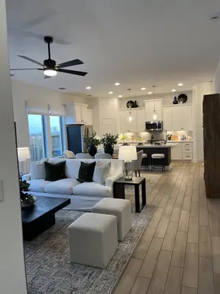 An inviting open-concept living room with sleek furnishings, natural light, and a spacious kitchen in the background.