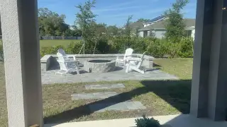 Model Home A cozy backyard patio with a stone fire pit and white Adirondack chairs, perfect for outdoor enjoyment.