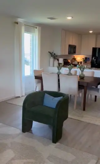 A cozy dining and living area with a green accent chair, sleek dining table, and modern kitchen fittings.