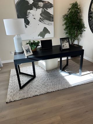 A modern office with a sleek black desk, abstract art, and a cozy rug on light wood flooring.