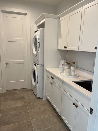 A sleek laundry room featuring a stacked washer-dryer, white cabinetry, and smooth countertops.