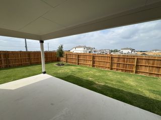 A covered patio overlooks a private fenced yard with fresh greenery and a small tree.