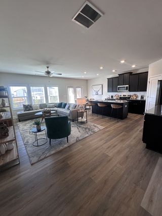 Model Home A modern open-plan living area with a sleek kitchen, cozy seating, and natural light-enhanced wooden flooring.