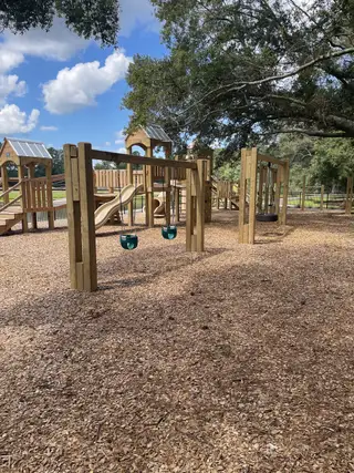 Community Amenities A charming playground with wooden swings and slides under lush trees in Six Oaks by Mungo Homes (Summerville, SC).