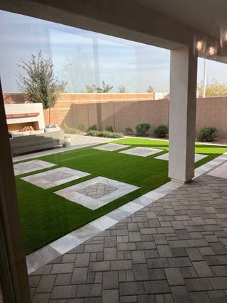 A modern outdoor space with geometric pavers, artificial turf, and a cozy seating area, ideal for relaxation.