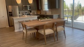 A modern kitchen with sleek cabinetry, stainless steel appliances, and a wooden dining set by large glass patio doors.