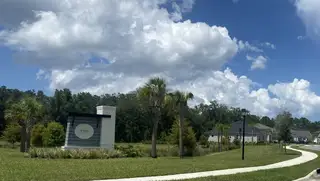 Street view A scenic entrance with lush greenery at RiverTown - Vista by Mattamy Homes in St. Johns, FL, under a vibrant blue sky.