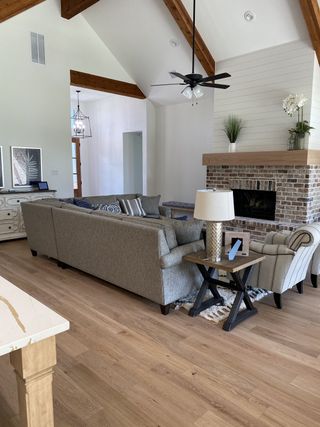 A cozy living room with wooden beams, a brick fireplace, and comfortable seating, accented by soft, neutral tones.