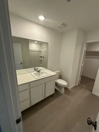 A modern bathroom with sleek white cabinetry, large mirror, and ample storage leading to a spacious closet.
