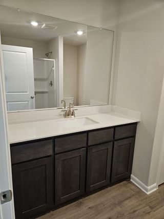 A modern bathroom features a sleek countertop, large mirror, dark wood vanity, and bright lighting.
