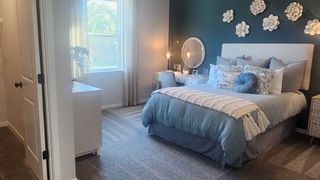 A cozy bedroom with teal accent wall, plush bedding, decorative wall flowers, and a bright vanity area.