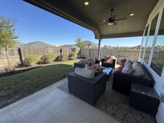 A cozy covered patio features stylish wicker furniture, plush cushions, and serene views of a fenced yard and greenery.