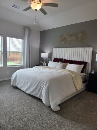 Model Home A cozy bedroom featuring a plush white bed, gray accent wall, elegant decor, and natural light from large windows.