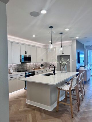 A modern kitchen with sleek cabinetry, a large island, pendant lights, and herringbone flooring.