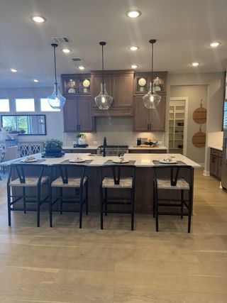 A modern kitchen featuring wooden cabinets, an island with seating, pendant lighting, and sleek countertops.